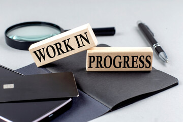 WORK IN PROGRESS text on wooden block on black notebook , business concept