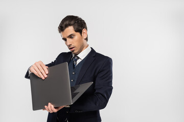 shocked businessman in suit looking at laptop isolated on grey