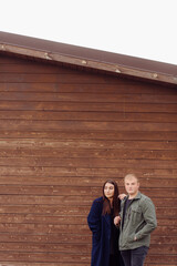 Young beautiful couple in fashionable clothes standing near a wooden wall.