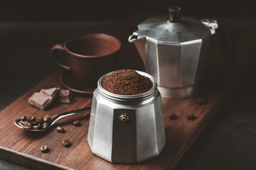 Moka coffee pot filled with brown ground coffee on dark wooden board, prepare to brewing Italian...