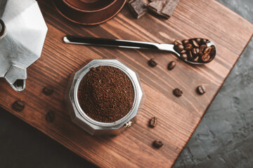 Moka coffee pot filled with brown ground coffee on dark wooden board, prepare to brewing Italian...