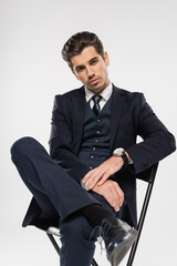 businessman in formal wear sitting on chair while posing isolated on grey