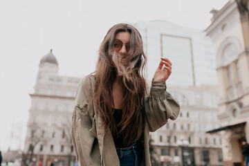 Fototapeta premium Outdoor photo of excited lovely girl with loose hair dancing, listening music and having fun in the city. 