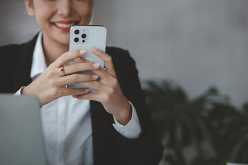 Beautiful Asian woman playing mobile phone in her break from work, she is a marketing manager of a startup company, female leader, supervisor, ceo. Female Leadership Concept.