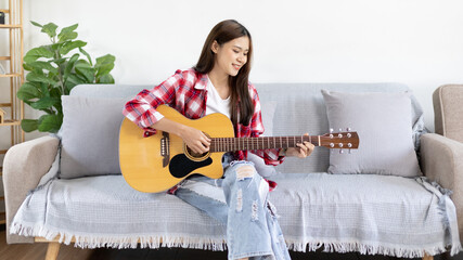 Asian female artist playing the guitar and singing happily in the living room, Relaxation with...