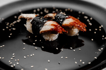 Two portions of sushi with shrimp and eel on a black plate on a gray background
