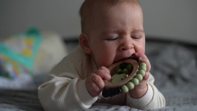 baby chewing teether toy. Infant growing first tooth. Boy biting toy on parents bed. Pretty six-month old baby boy. Realistic toddler home portrait