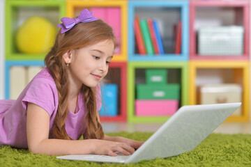 Teenage girl with laptop lying on carpet at home