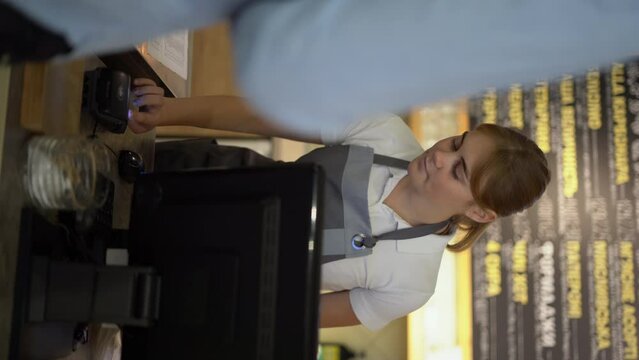 Smiling waitress barista saleswoman on coffee shop counter, man client pay in cafe with phone via pos machine using nfc terminal make contactless mobile payment.
