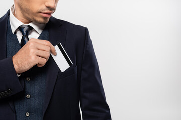 cropped view of young businessman in suit putting credit card in pocket isolated on grey
