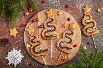 Christmas tree shape puff pastry cakes with chocolate filling and sugar powder. Delicious homemade New Year sweet baking. 