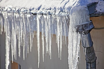 Big icicles on snow covered old roof with downpipe intake on city  house at Sunny winter day in Europe - obrazy, fototapety, plakaty