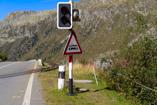 Crossing of railway track and mountain pass road with warning light at Swiss mountain pass Furkapass on a sunny late summer day. Photo taken September 12th, 2022, Furka Pass, Switzerland.