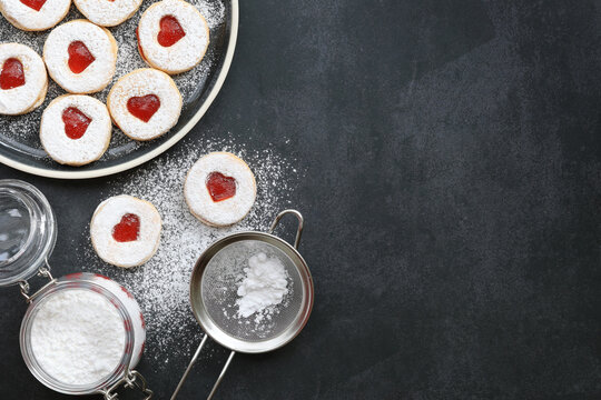 A plate of cookies, a jar of powdered sugar and colander on dark background