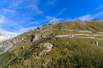 Obraz premium Aerial view of mountain panorama in the Swiss Alps at region of Swiss mountain pass Furkapass with serpentine road on a sunny summer day. Photo taken September 12th, 2022, Furka Pass, Switzerland.