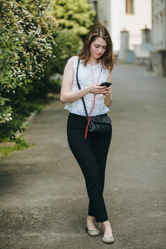 Happy beautiful young Caucasian girl with smart phone outdoors on sunny summer day texting and smiling