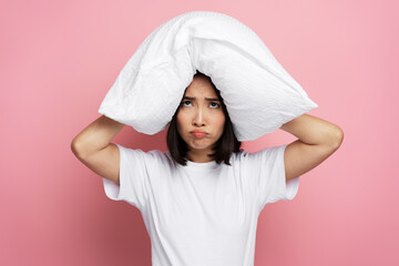 Annoyed angry woman closes her ears with pillow in morning because of noise