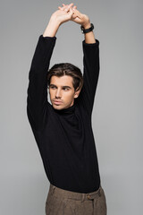 young good looking man in black turtleneck posing with raised hands isolated on grey