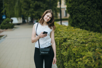 Happy beautiful young Caucasian girl with smart phone outdoors on sunny summer day texting and smiling