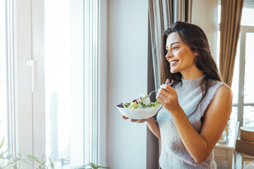 Healthy diet. Beautiful woman on the sofa eating a healthy salad. Beautiful healthy woman eating lettuce. Girl eating organic fresh salad. Close-up of a smiling woman eating a salad in the living-room