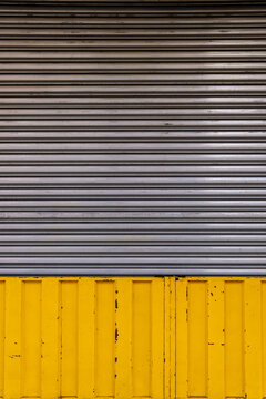 Vertical old grey corrugated metal garage and store door with yellow frame