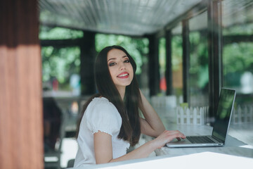 Portrait of beautiful smiling brunette woman sitting in a cafe with laptop outdoor.