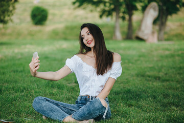 Fototapeta premium Young brunette woman, girl working with laptop, tablet and phone in green field, park with sunshine