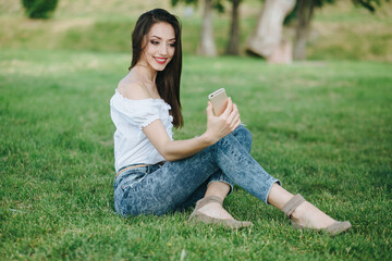 Young brunette woman, girl working with laptop, tablet and phone in green field, park with sunshine
