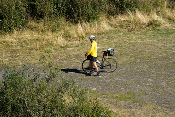 Male cyclist pushing his bicycle over meadow in the Swiss Alps at region of Muttbach, Canton Valais, on a sunny late summer day. Photo taken September 12th, 2022, Furka Pass, Switzerland.