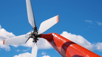 The white tail rotor of a bright red helicopter against a cloudy blue sky. Propeller on tail of a...