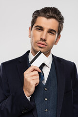 successful businessman in suit holding credit card and looking at camera isolated on grey