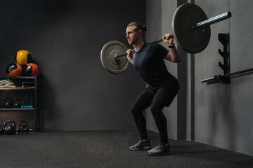 Fototapeta na wymiar Man lifting barbell as a part of crossfit training in dark workout gym. Space for text