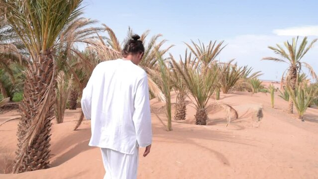 Spanish man with traditional moroccan dress walks around the palm trees
