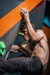 Fototapeta na wymiar A young, athletic guy with a beautiful inflated body climbs a bouldering in a climbing hall. Emotions on the face.