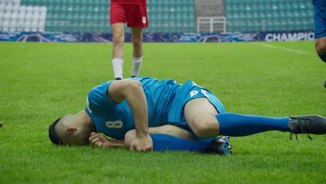 Professional Soccer Football Match Championship: Blue Team Players Attacks, Loses Ball to Foul. Action Game on an International Tournament. Slow Motion Athlete In Pain Lying on the Grass after Falling