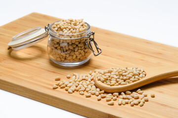 Pine nuts on a wooden board. Wooden spoon with pine nuts on the background of a jar of nuts....