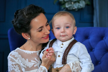 Happy mother with little son near Christmas background. Female in white dress sit at blue sofa and hugging baby . Small charming baby boy. happy motherhood concept. New Year and Christmas holidays.