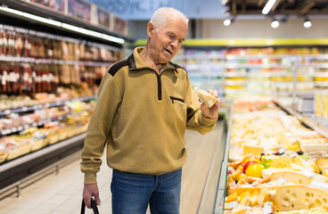 elderly man choosing cheese in supermarket