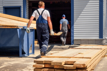 Two workers wear wooden planks on sawmill or in carpentry shop. Authentic workflow. Timber...