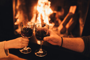 Happy couple drinking red wine sitting by the fire in front of cozy fireplace.