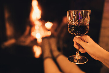 Young woman drinking red wine sitting by the fire in front of cozy fireplace.