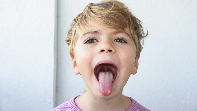 Preschool child widely open mouth showing a tongue stuck out as far as possible, with a clear view on the uvula and the soft palate. Epiglottis and the consistency of saliva are visible.