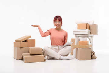Beautiful  Asian girl in glasses is sitting on the floor. Packaging boxes are standing nearby. Moving to a new house, packing. Isolated on white background. Ad, moving and delivery concept
