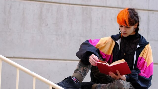 Young woman with orange and black hair, reading a red book.