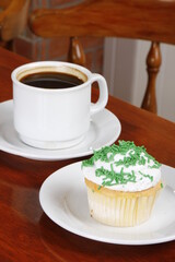 Creamy cupcake with green sprinkles and hot chocolate on the table