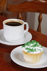 Creamy cupcake with green sprinkles and hot chocolate on the table