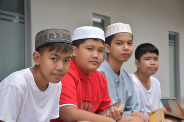 Portrait asian muslim or islamic boys sitting with muslim boys in a row to pray or to do the religious activity, soft and selective focus.