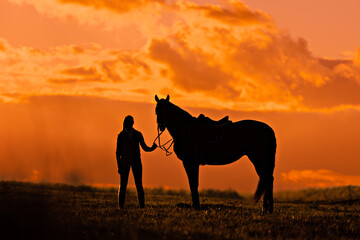 Silhouette of a woman with horse at the orange sunset