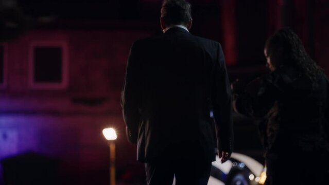 Team of Two Multiethnic Police Officers Working on Profiling a Killer on the Loose. Detectives on Duty at Night Solving Crime to Bring a Violent Murderer to Justice. Police Car and Paramedics on Site