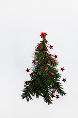 Christmas tree made of an evergreen tree branch and red stars on white background. New Year minimal concept.